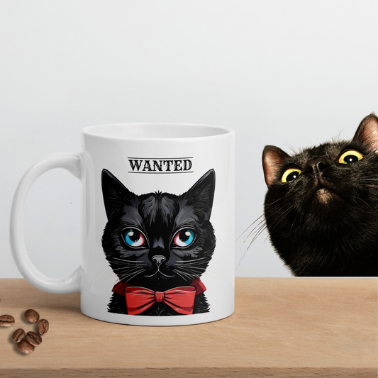 Glossy white ceramic black cat mug with an adorable black cat and a humorous "Wanted" message printed on it, placed on a bench with coffee beans, while a cute black cat peeks from behind.