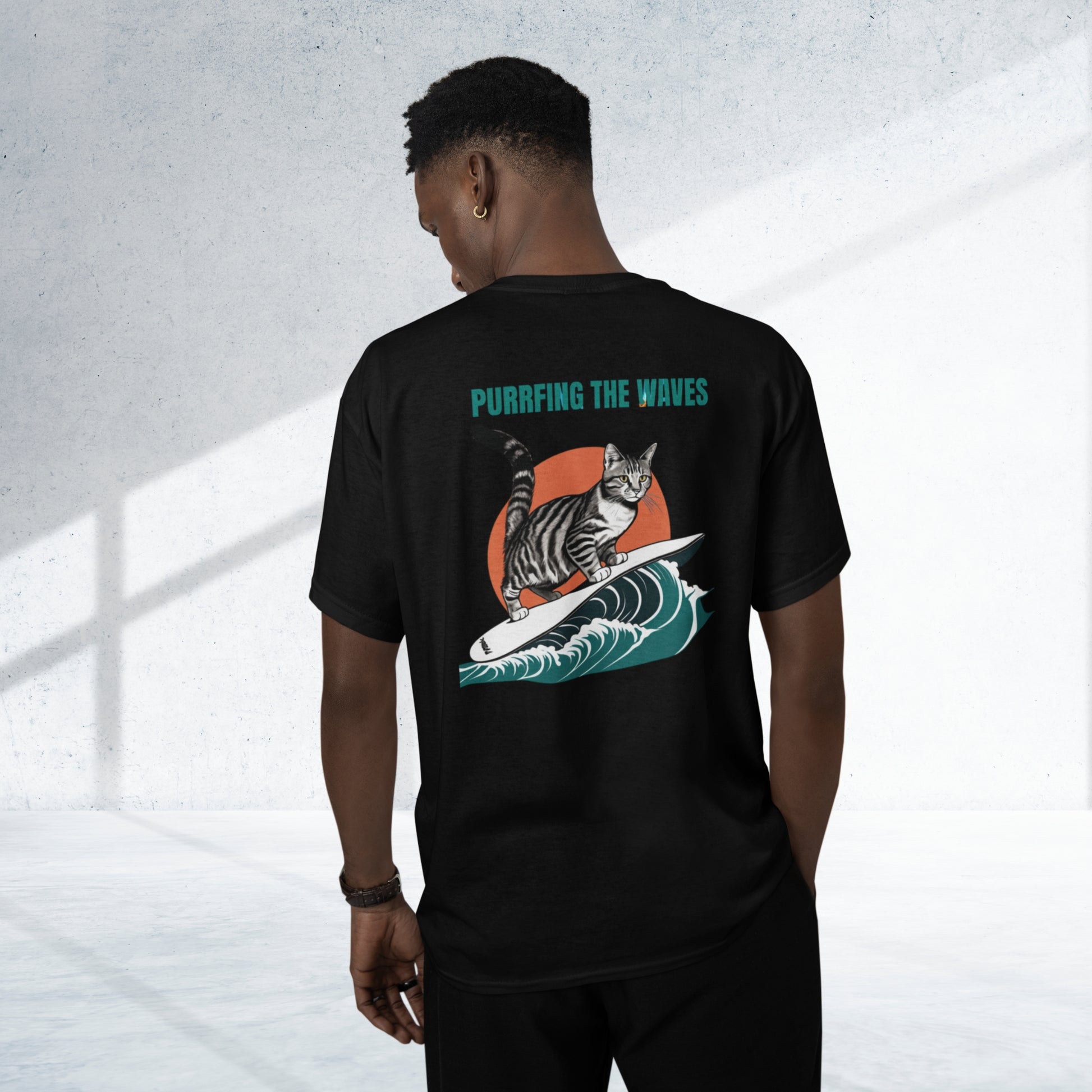 Back view of a young man wearing a black funny cat tee shirt, featuring a playful surfing cat design and the text: 'Purring the Waves' printed on it. A cool and humorous design for cat lovers!