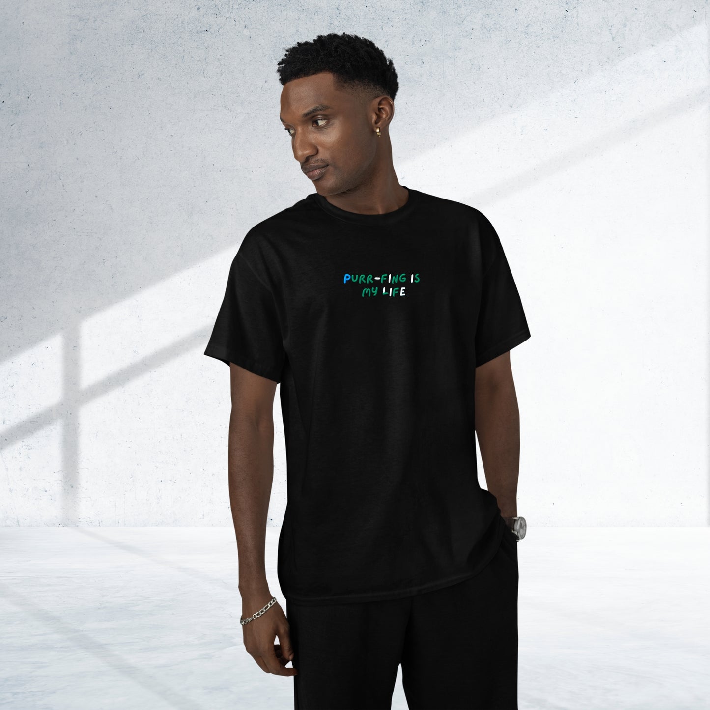 A young man wears a stylish black cotton short-sleeve t-shirt, with an amusing design featuring 'Purr-fing is my life!' on the front, exuding joy and humor.