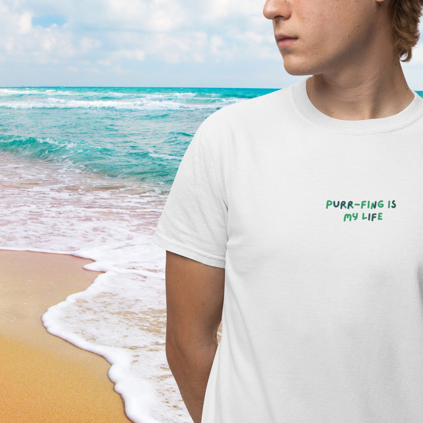 A young man wears a stylish white cotton short-sleeve t-shirt, with an amusing design featuring 'Purr-fing is my life!' on the front, exuding joy and humor.