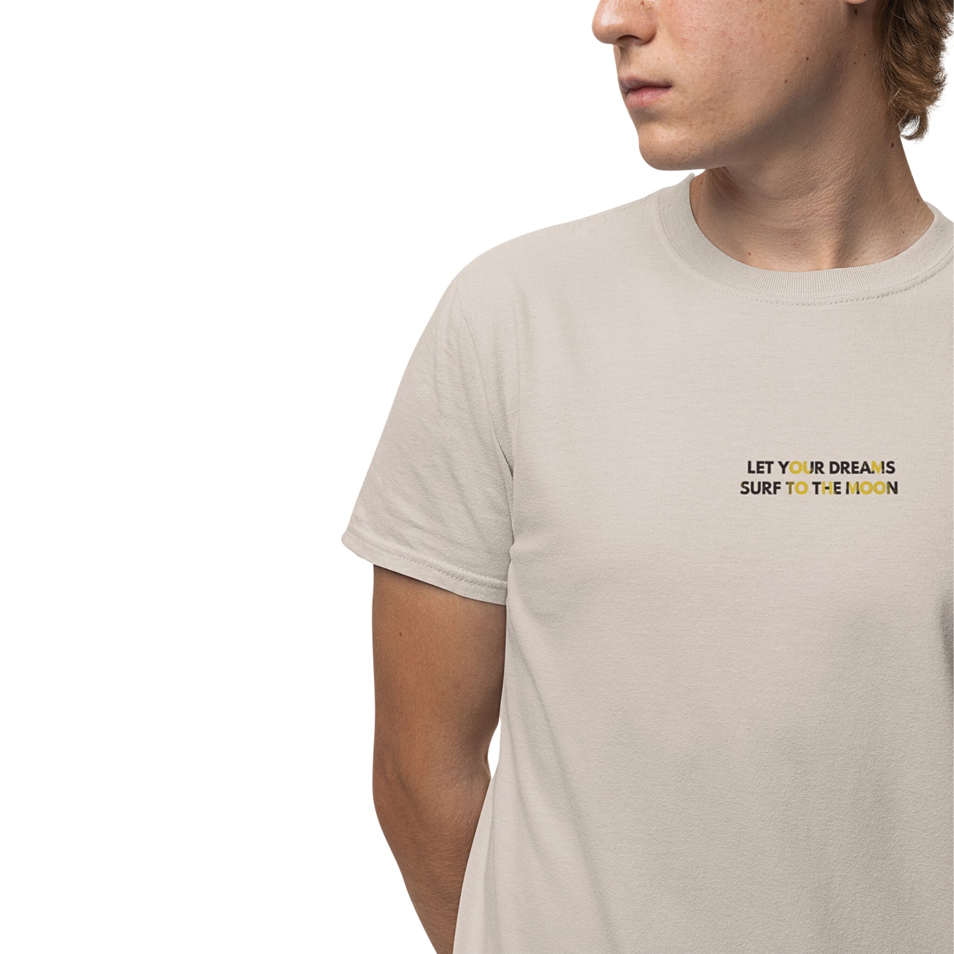 A young man wearing a natural-colored cotton T-shirt with a 'Let Your Dreams Surf to the Moon' graphic on the front.