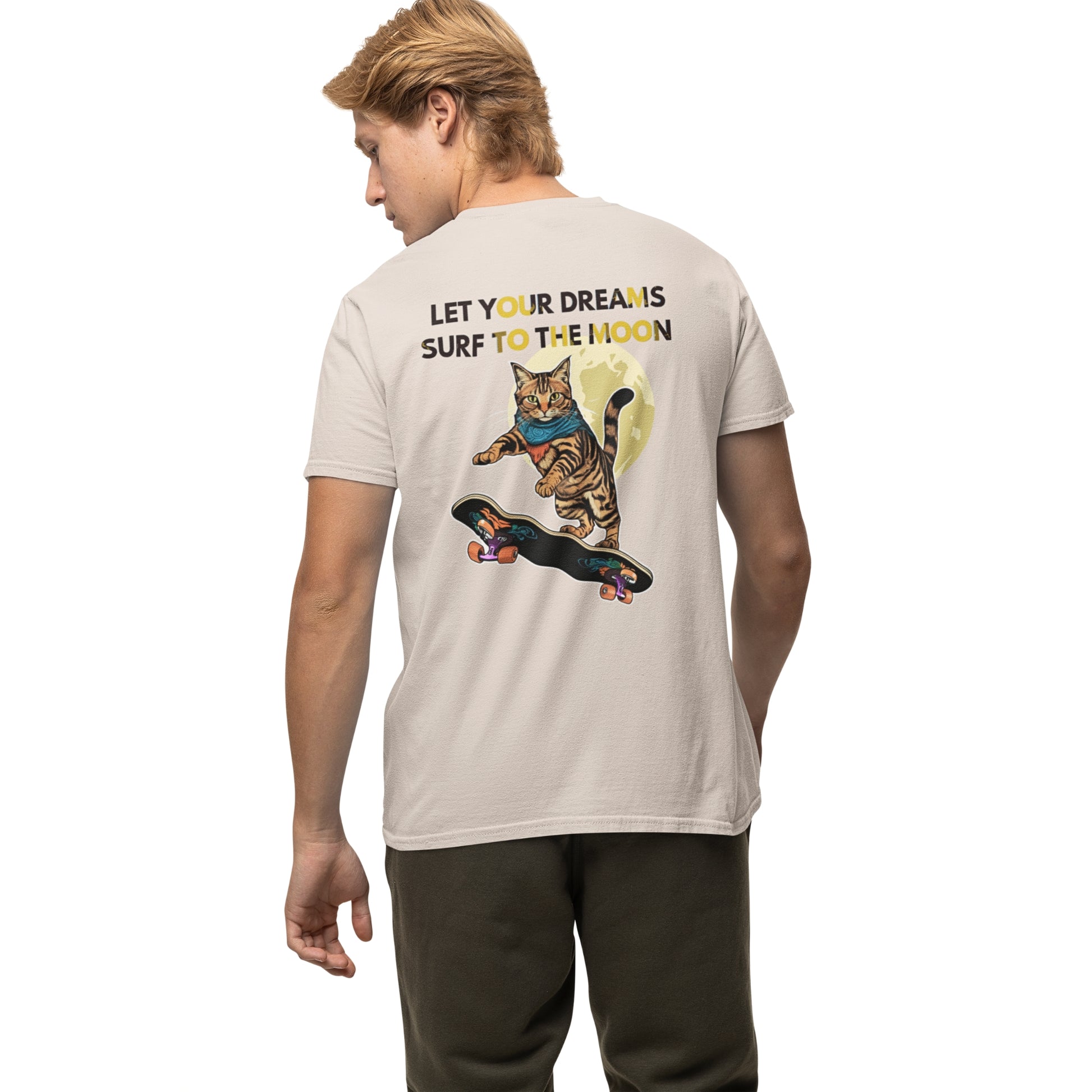Back view of a young man wearing a natural-colored cotton T-shirt featuring a cat skateboarding toward the moon graphic.