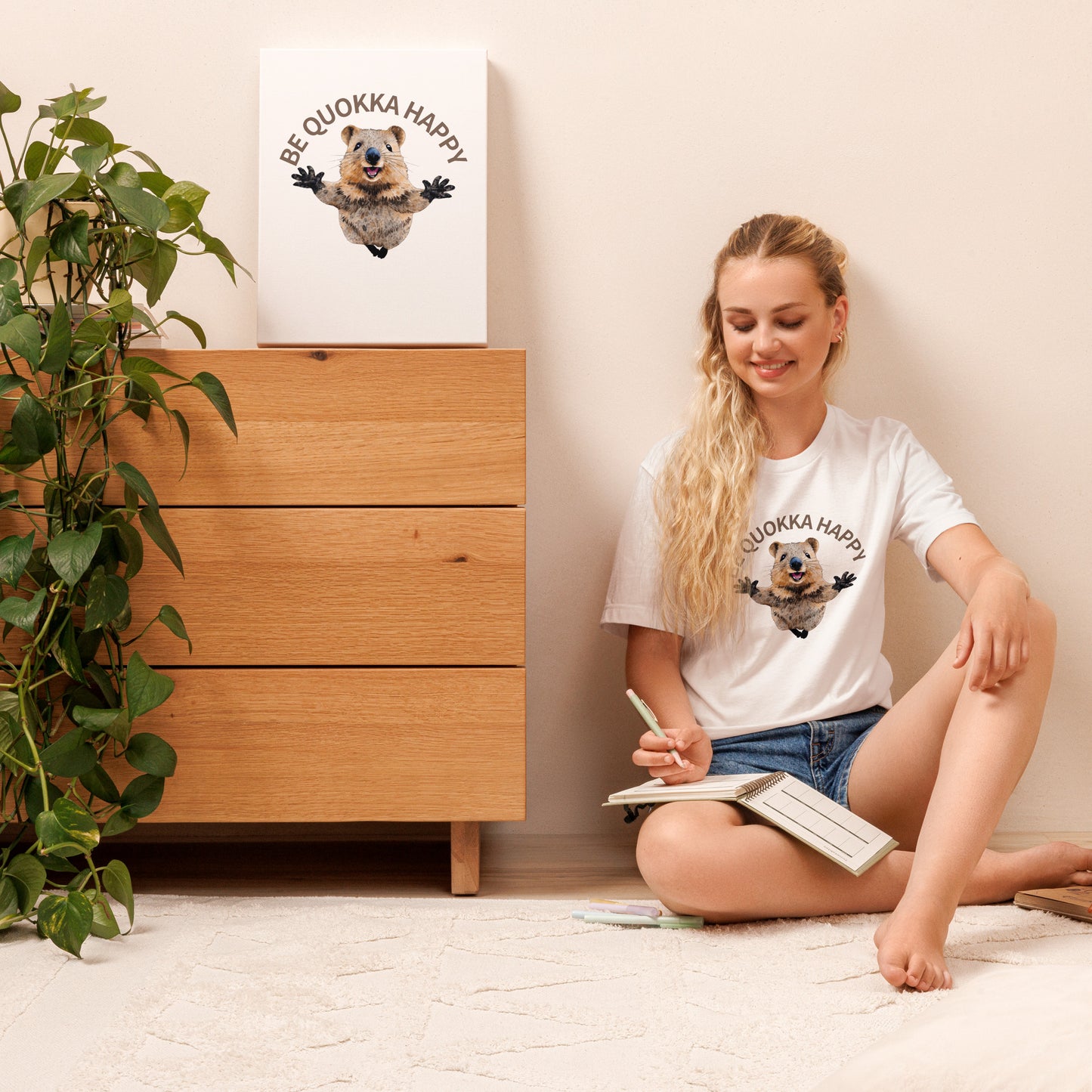 A young girl wearing a white cotton T-shirt with a Happy Quokka graphic, sitting on the floor in a stylish modern room.