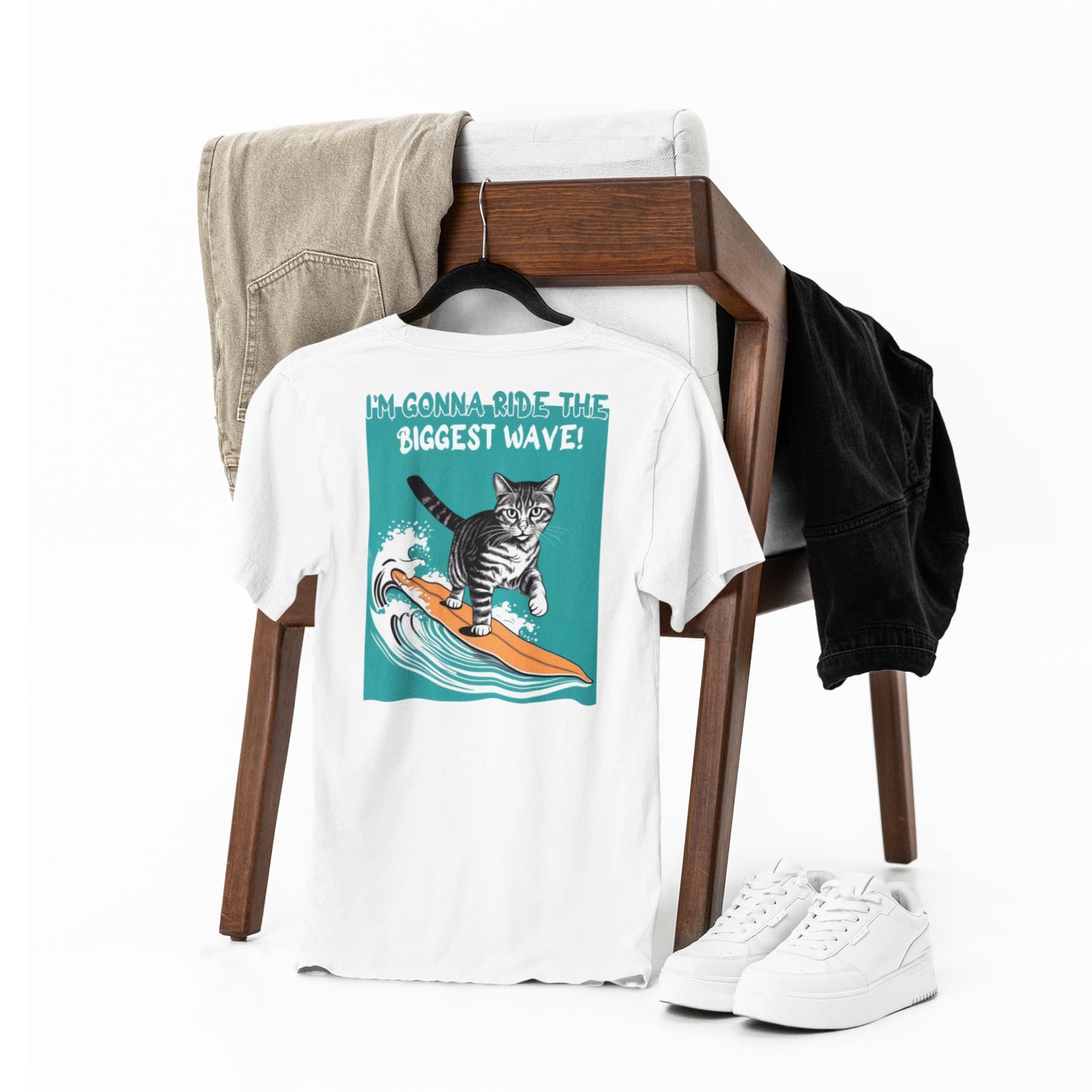An white cotton cat funny t-shirt hanging on a chair, featuring a playful graphic of a waving cat and the text: 'I'm gonna ride the biggest wave' on the back. A cool and humorous design for cat lovers.