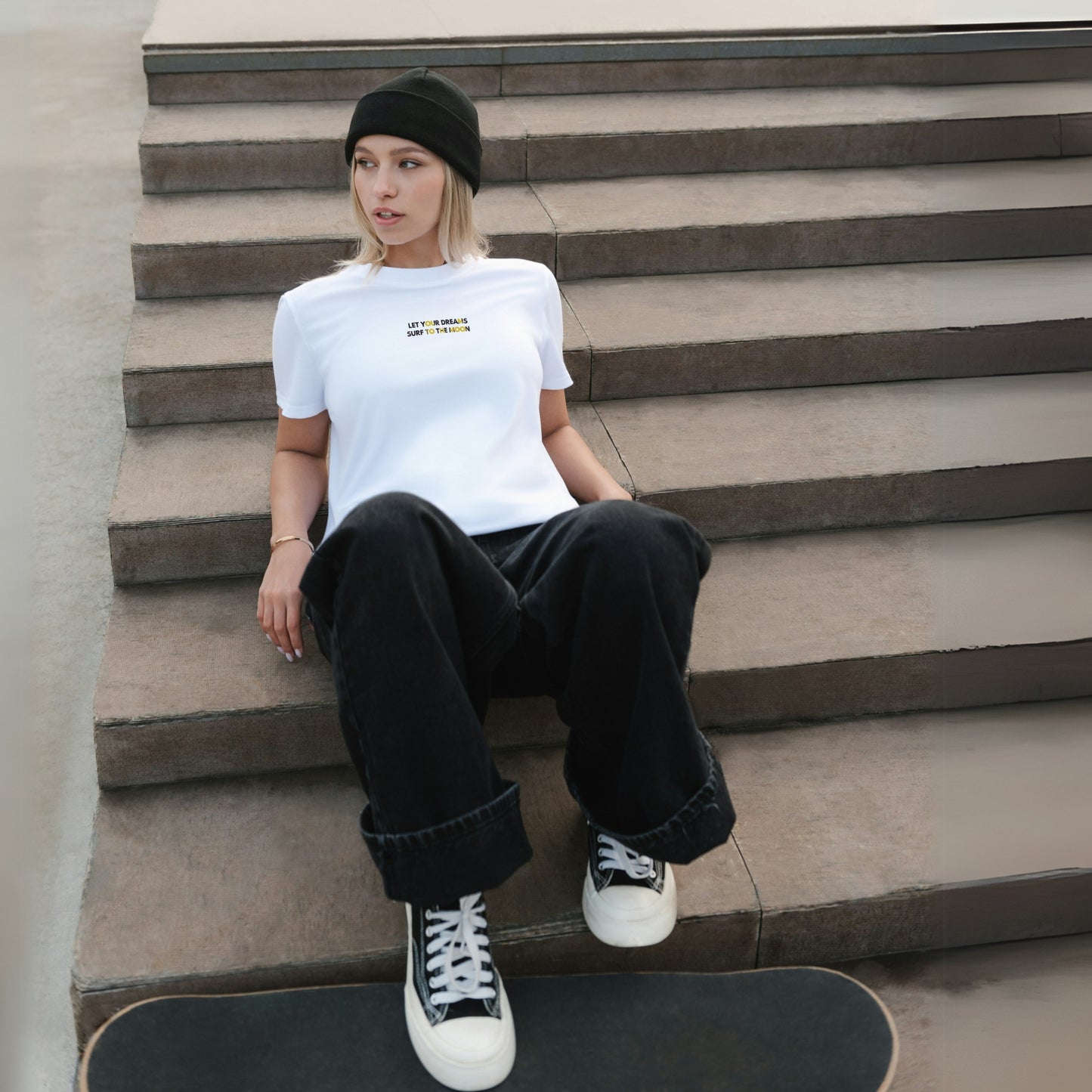 A young girl wears a white cotton T-shirt with a simple yet dynamic phrase printed on the front of her chest. She stands with a skateboard under her feet, exuding a cool and casual vibe.
