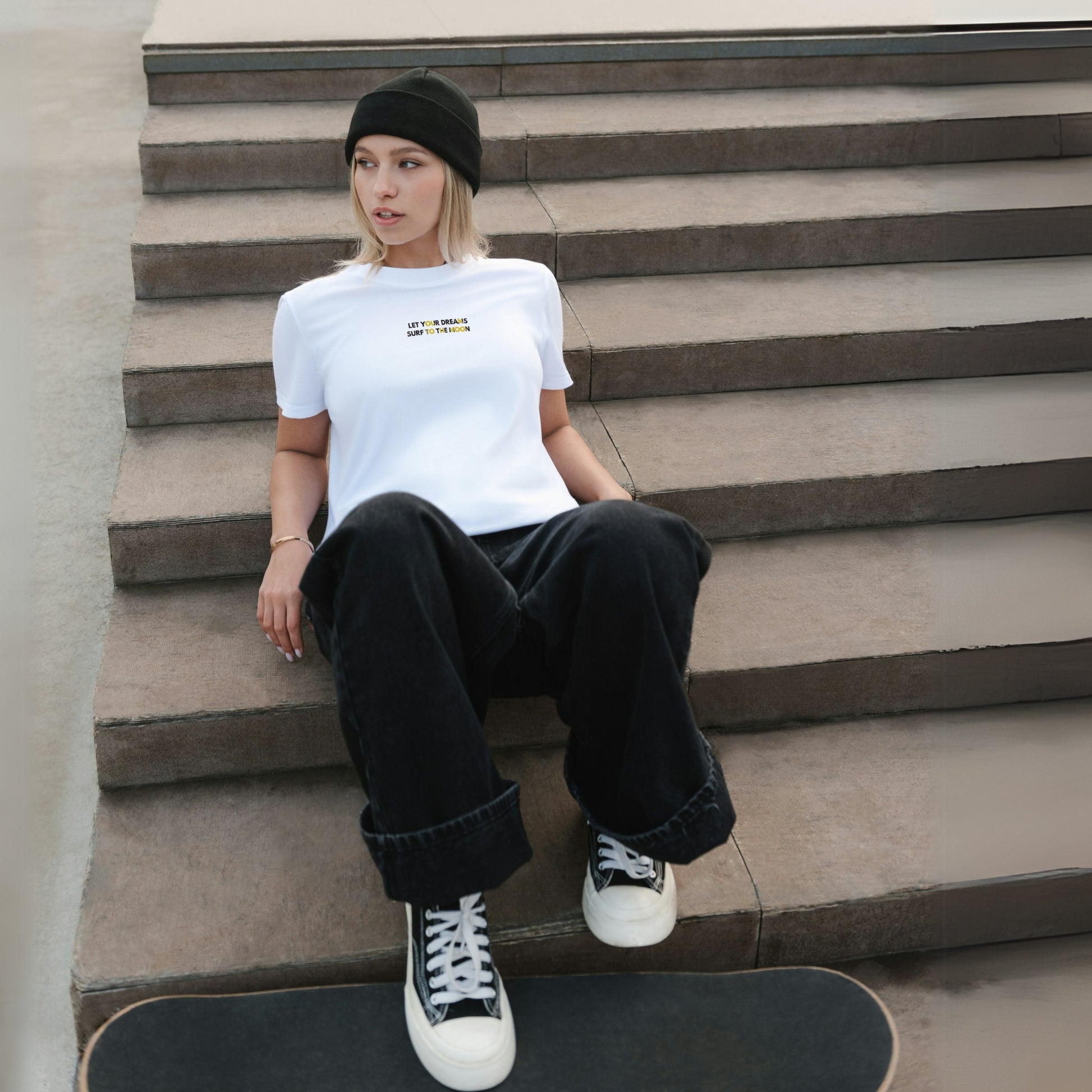 A young girl wears a white cotton T-shirt with a simple yet dynamic phrase printed on the front of her chest. She stands with a skateboard under her feet, exuding a cool and casual vibe.